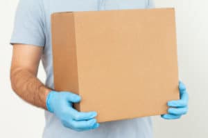 Delivery man holding cardboard box in medical rubber gloves